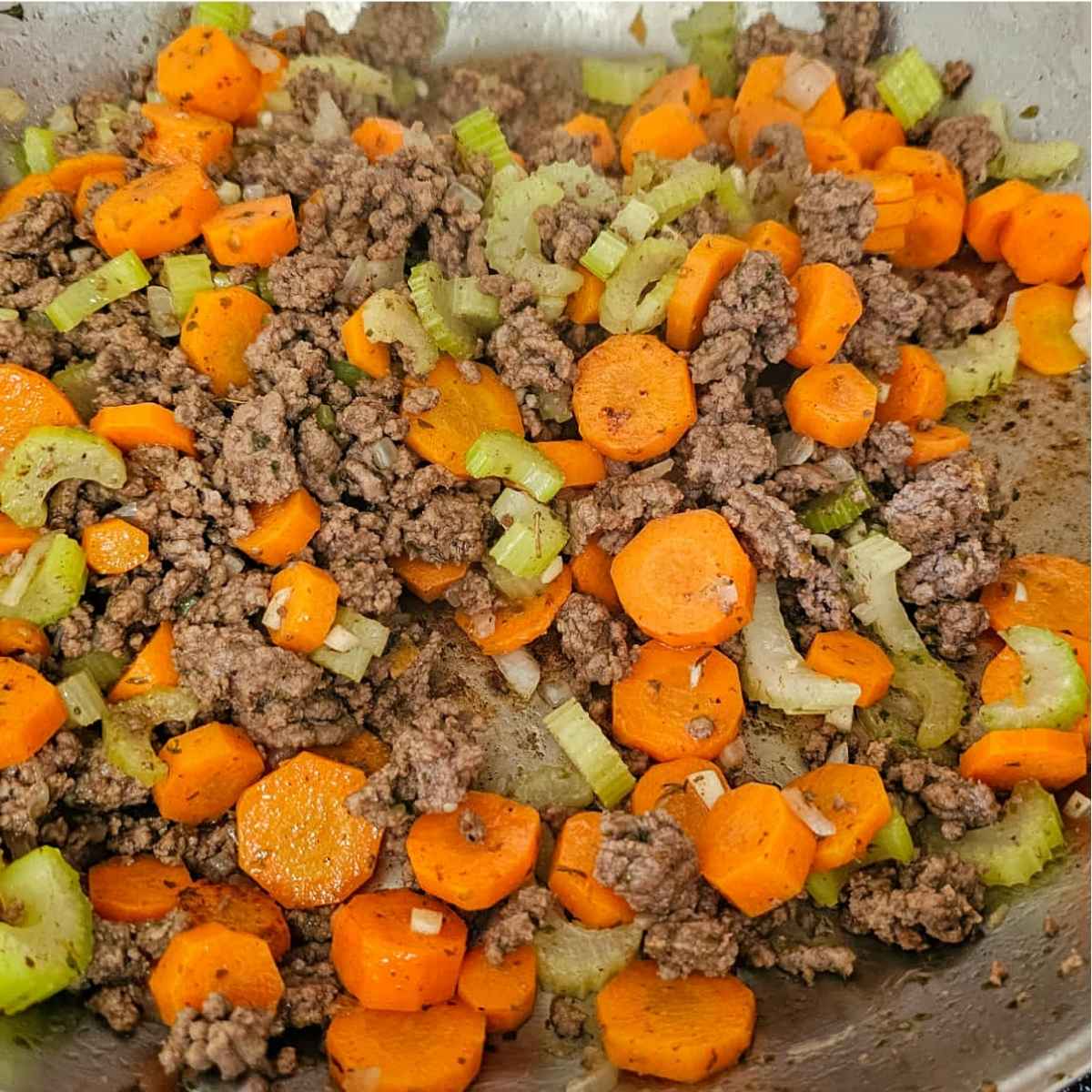 ground beef, carrots, onions, celery and garlic cooking in a pan