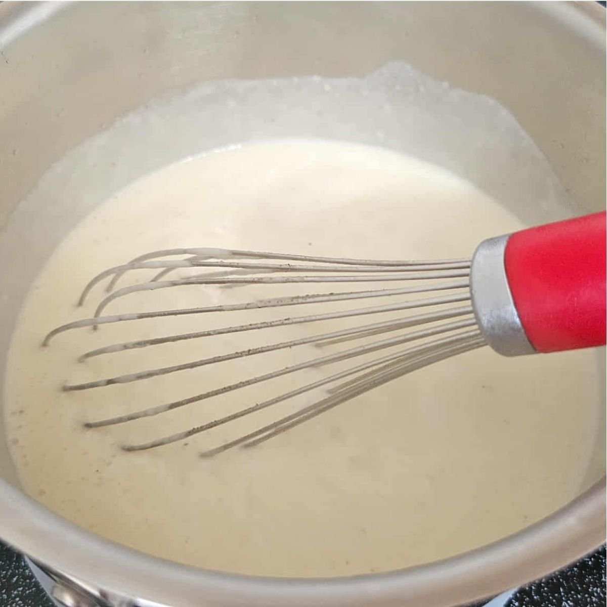 roux in a small stainless steel pot coming to a boil with a whisk
