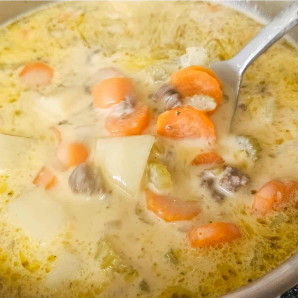 cheeseburger soup in a medium pot being scooped out with a spoon