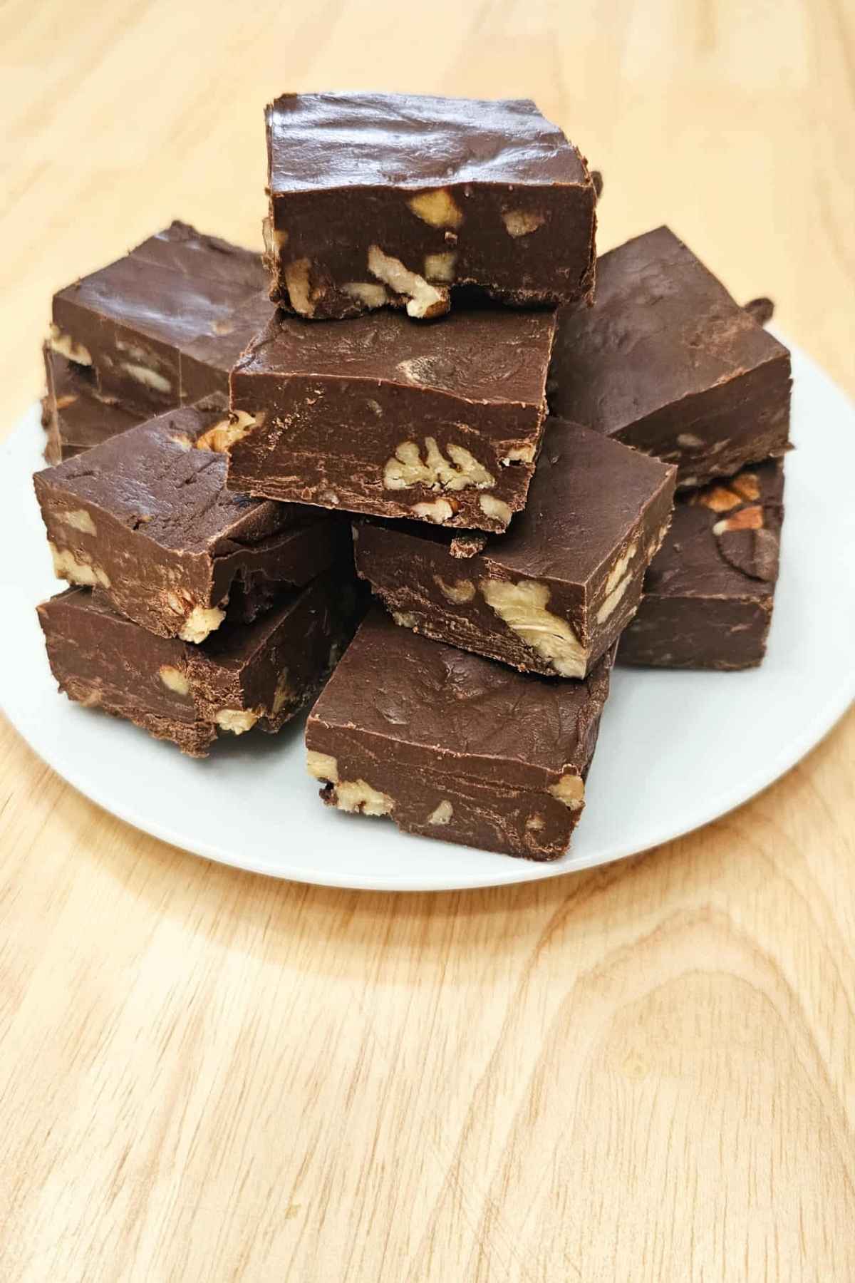 a pile of chocolate pecan fudge sitting on a white plate on a wooden counter top