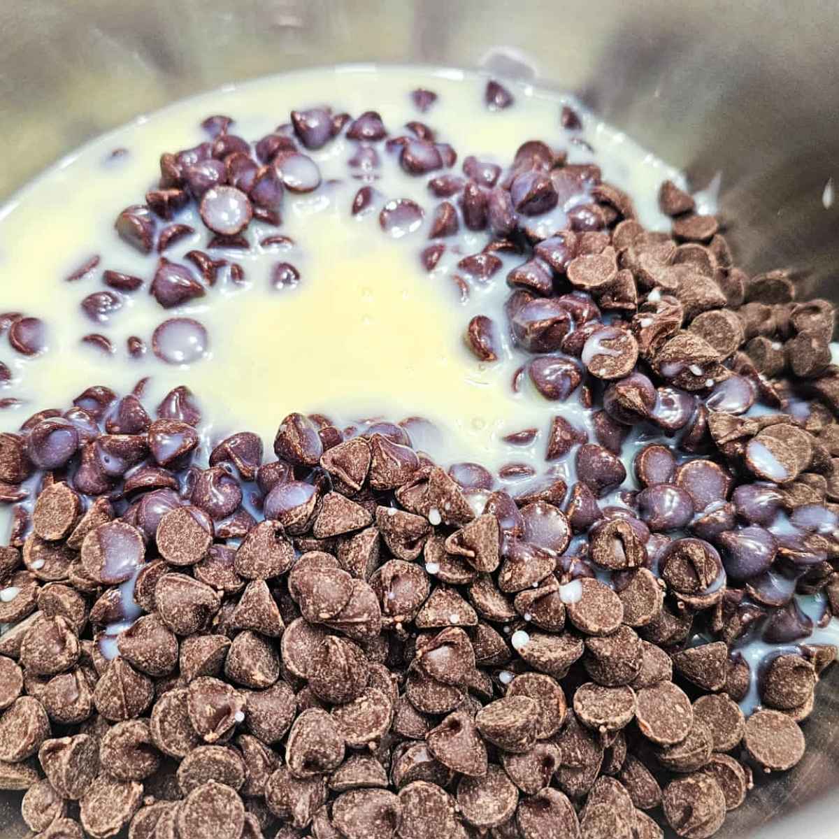 chocolate chips and sweetened condensed milk sitting in a medium stainless steel pot melting into each other