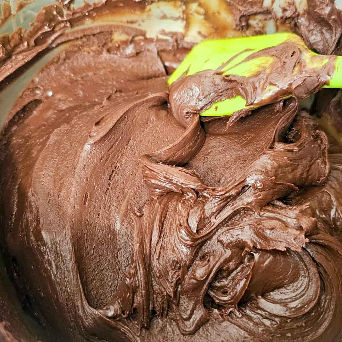 chocolate chips melted in sweetened condensed milk in a medium stainless steel pot with a green rubber spatula in it