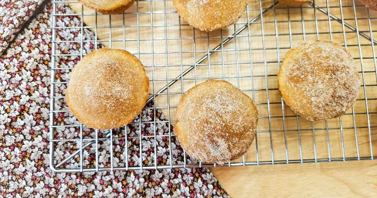cinnamon sugar muffins on a wire rack cooling on a wooden table with a fall cloth napkin to the side of it