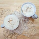 2 glasses of hot maple milk sitting on a doily on a wooden table
