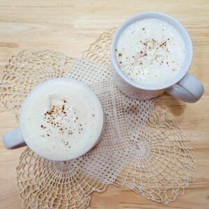 2 glasses of hot maple milk sitting on a doily on a wooden table