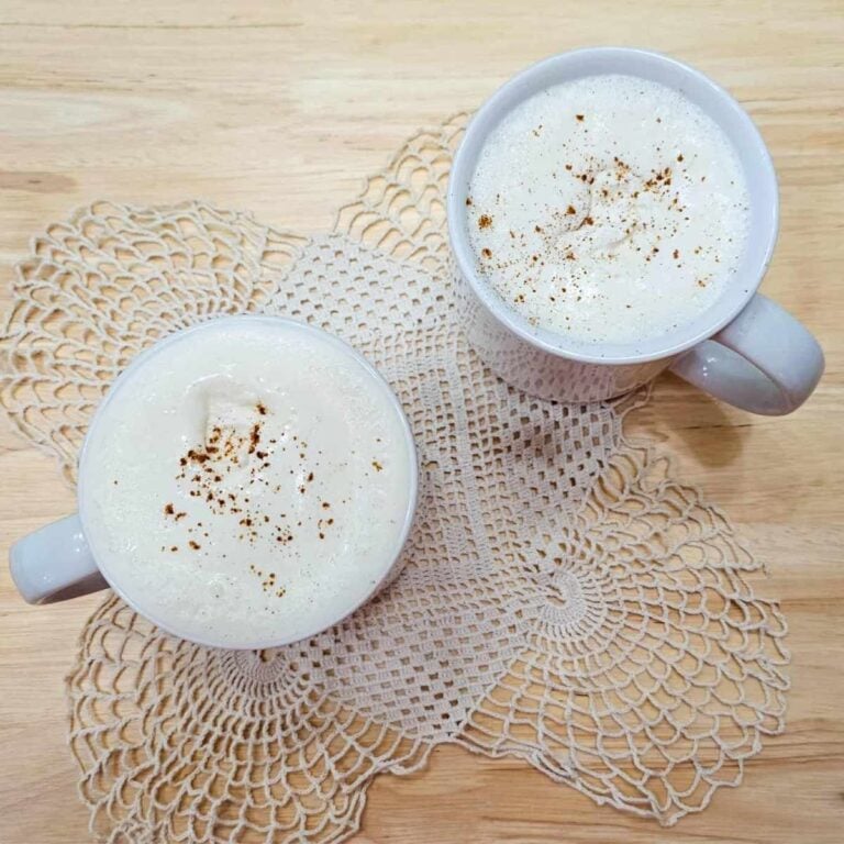 2 glasses of hot maple milk sitting on a doily on a wooden table