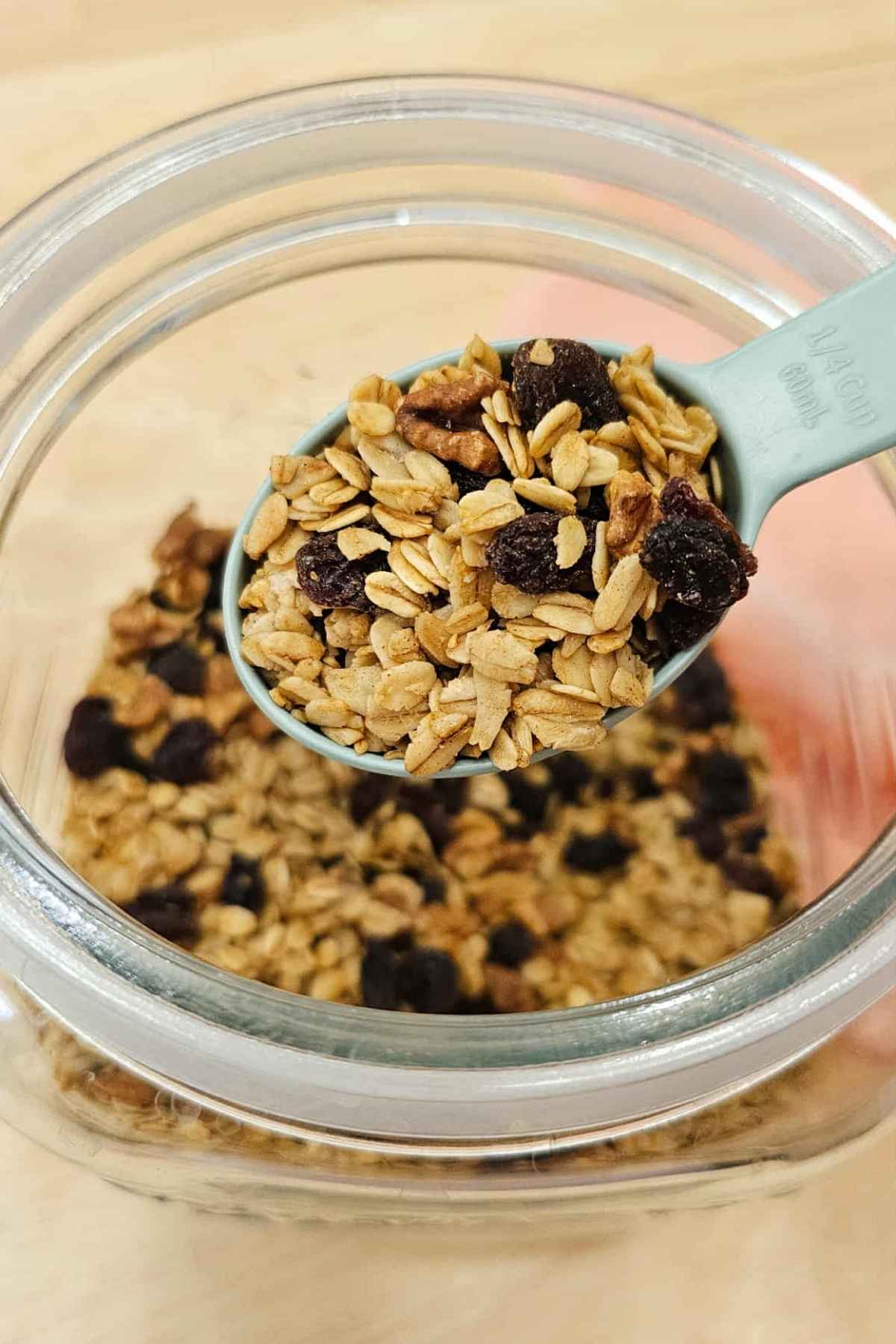 scooping out a 1/4 cup of maple walnut granola out of a glass storage container