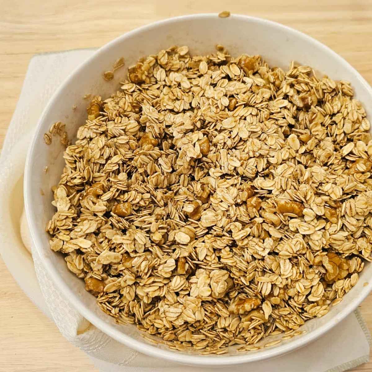 oats and walnuts with syrup poured over it and mixed together in a white glass bowl sitting on a wooden table