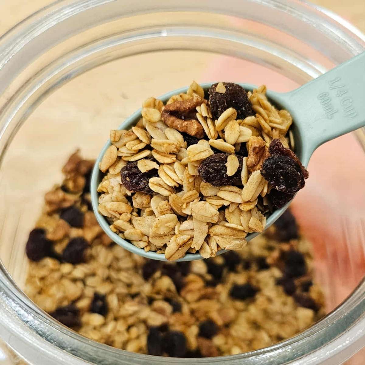 maple walnut granola in an air tight container being scooped out with a 1/4 cup measuring cup