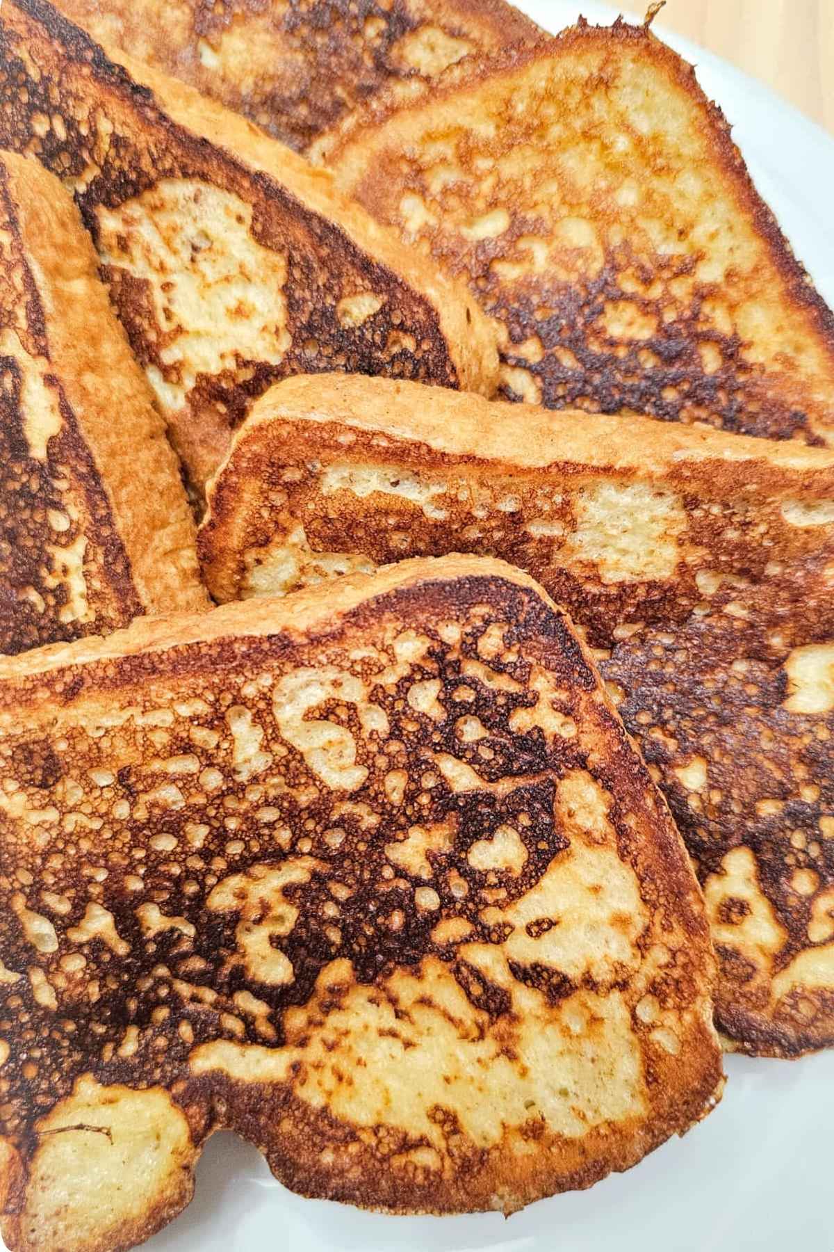 A pile of French toast close up and sitting on a white glass plate on a wooden counter top