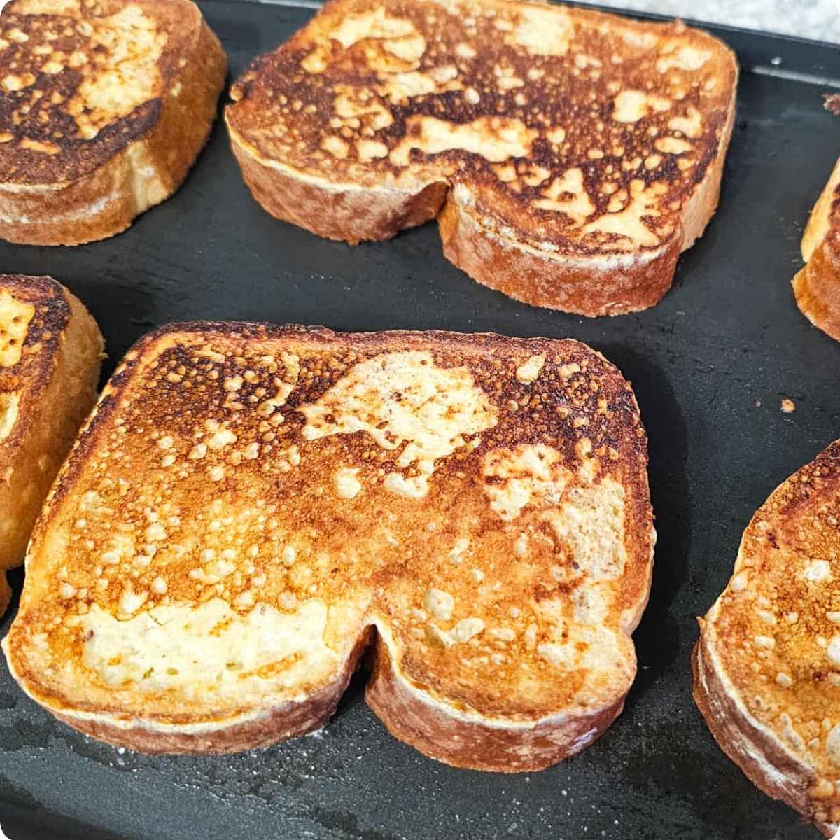 French toast cooking on the other side on an electric griddle that's sitting on a white and grey counter top