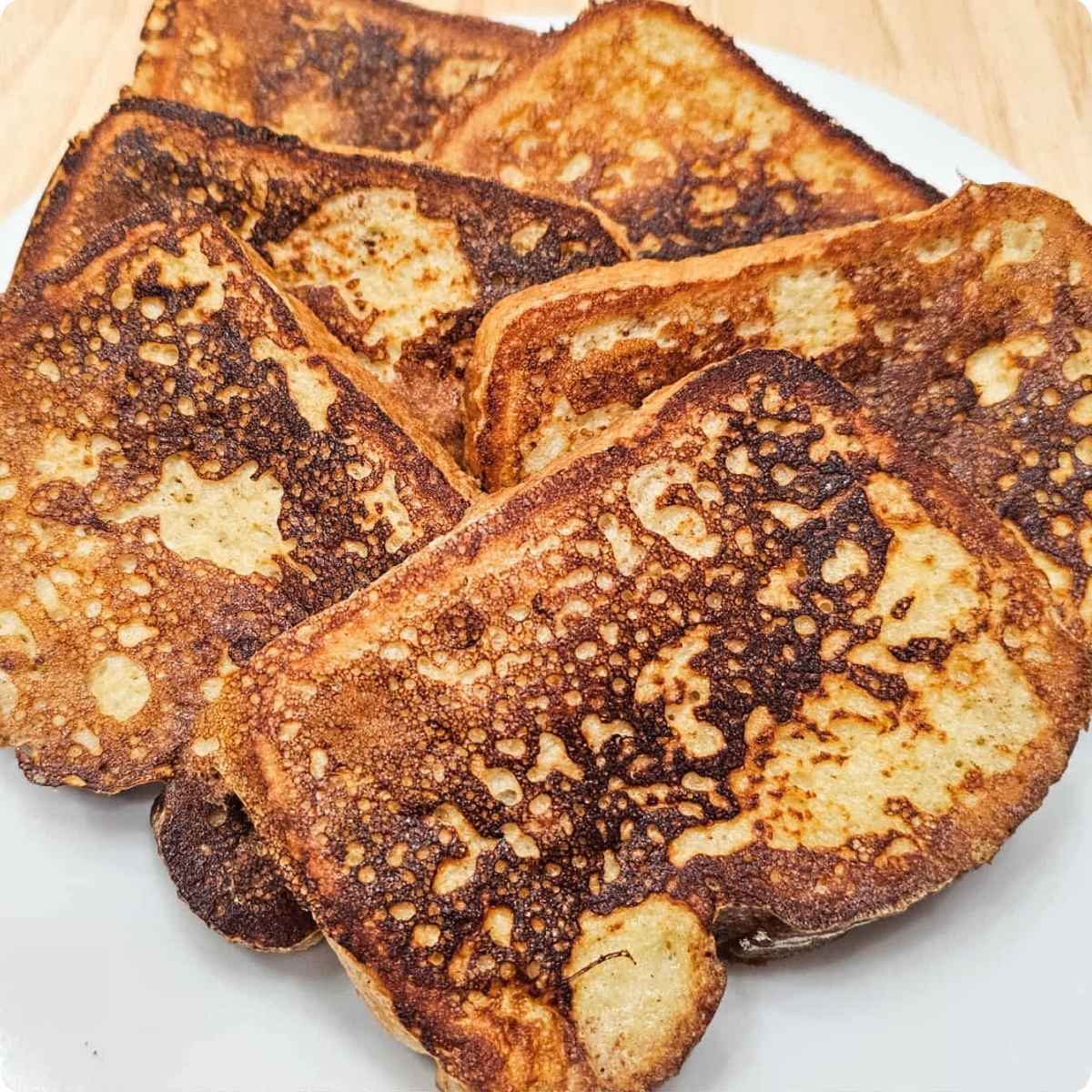 A pile of French toast sitting on a white plate on a wooden counter top