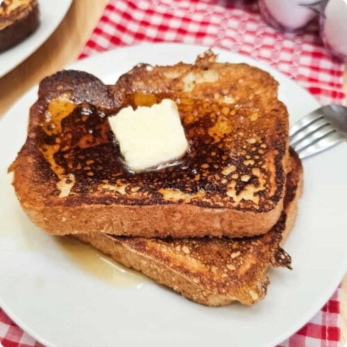 easy French toast recipe sitting on a white glass plate on a red and white checkered cloth napkin