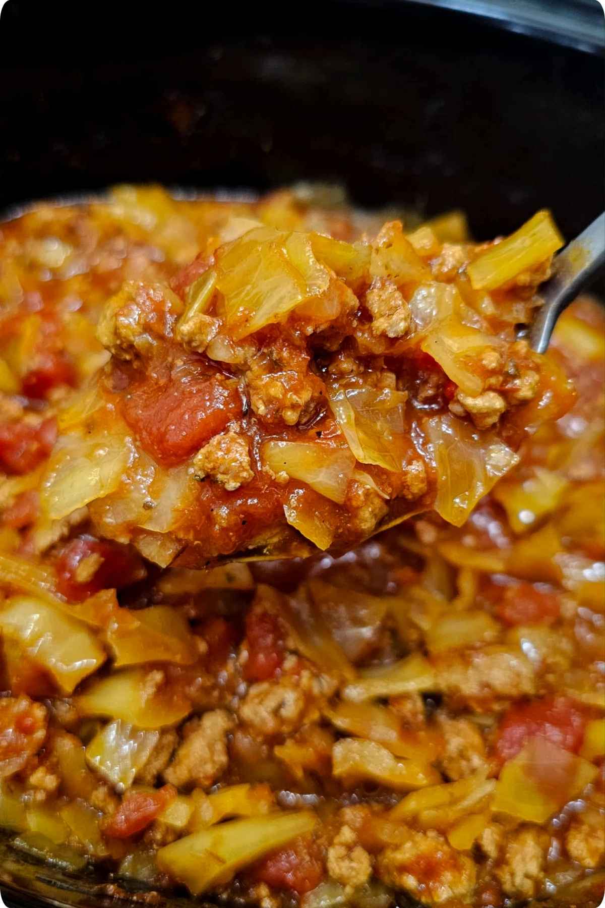 a close up of stuffed cabbage rolls being scooped out with a stainless steel spoon from the crock pot
