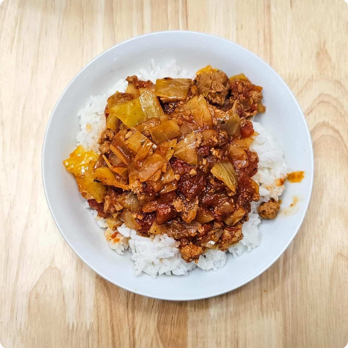 unstuffed cabbage rolls poured over hot rice in a white glass bowl sitting on a wooden counter top
