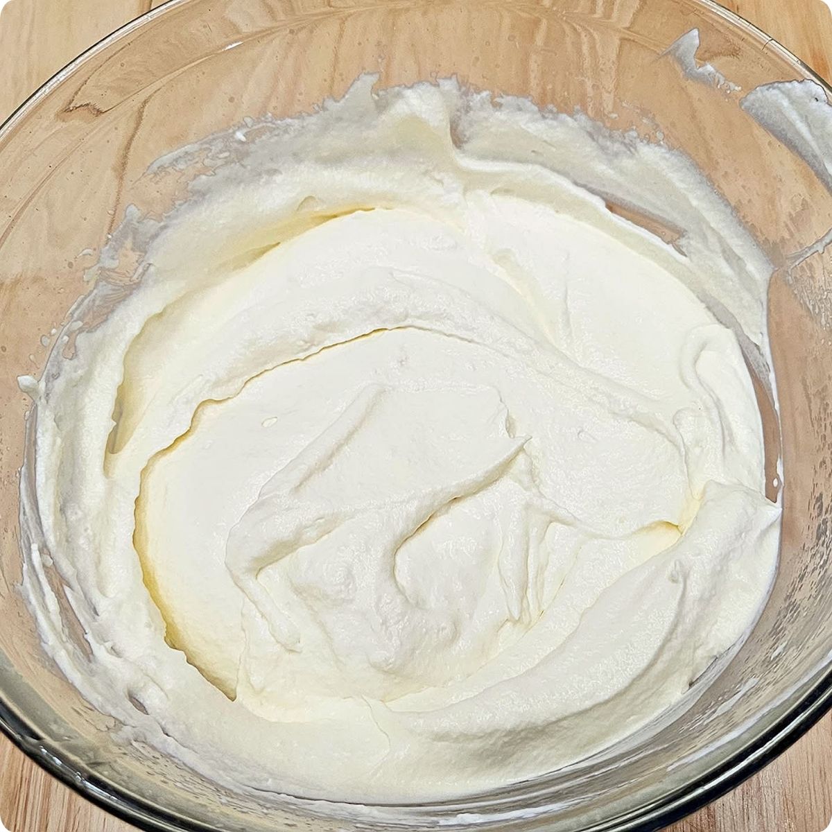 egg whites folded into the cream mixture sitting in a clear glass bowl on a wooden counter top