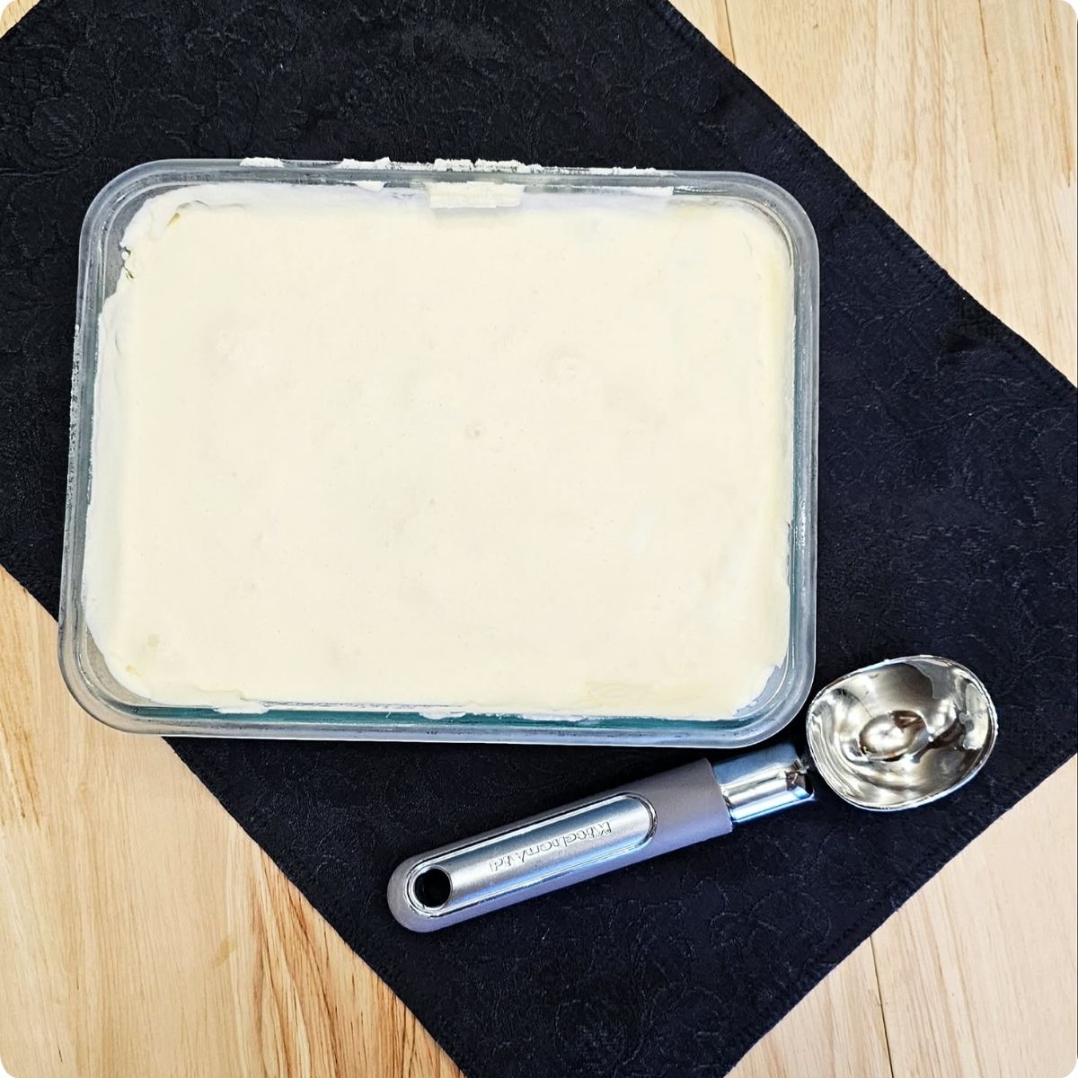 homemade no churn honey ice cream inside of a freezer safe container with an ice cream scoop next to it