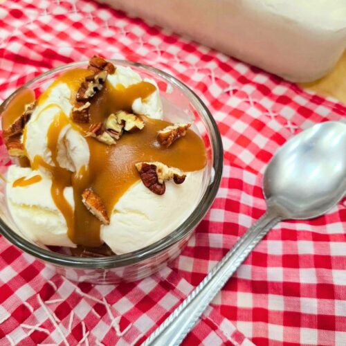 easy butterscotch sauce in a clear glass bowl sitting on a red and white table cloth with a spoon next to it